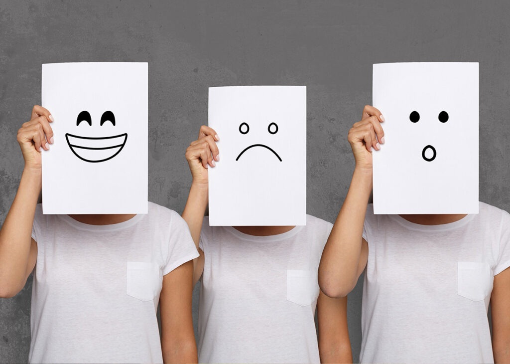 pessoa segurando um papel com desenho de rosto em tres tipos de emoções
