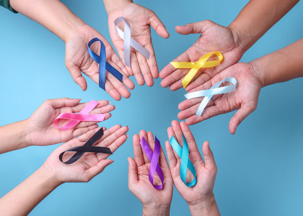 Várias mãos segurando laços de cores diferentes, representando as várias campanhas de combate ao câncer.